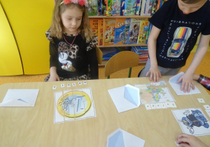 Dzieci układają przy stoliku obrazki z części oraz rozsypanki literowe.